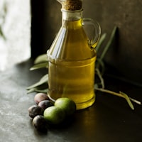 A corked glass bottle of golden oil beside fresh olives