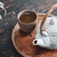 A cup of brewed tea on a wooden tray beside a white teapot