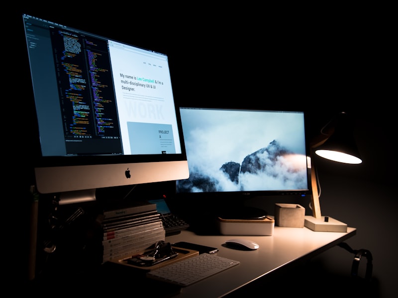 A desk at night with a code editor open on one monitor and a portfolio page on another